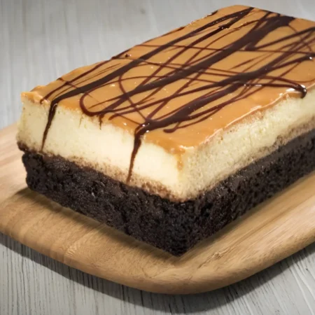 Chocoflan artesanal rectangular sobre tabla de madera con cobertura de arequipe e hilos de chocolate.