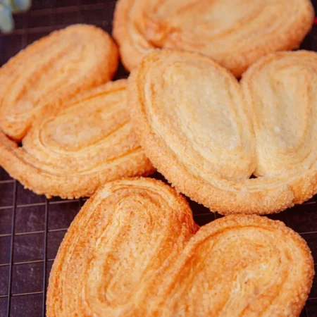 Corazones de hojaldre o palmeritas artesanales doradas y azucaradas sobre rejilla de enfriamiento.