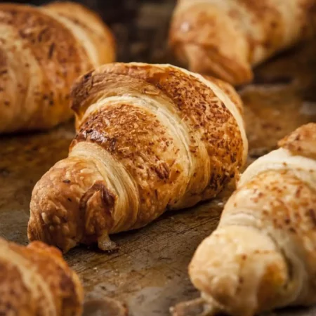 Croissants artesanales hojaldrados gratinados con queso y rellenos de jamón y queso.