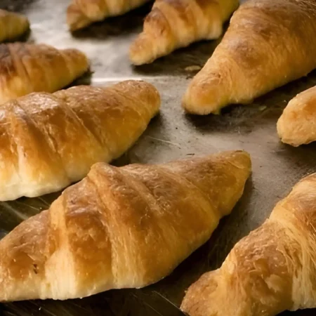 Croissants de mantequilla recién horneados sobre bandeja con capas hojaldradas doradas y crujientes.