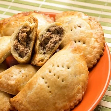 Empanadas de hojaldre doradas y crujientes rellenas de carne en un plato naranja.