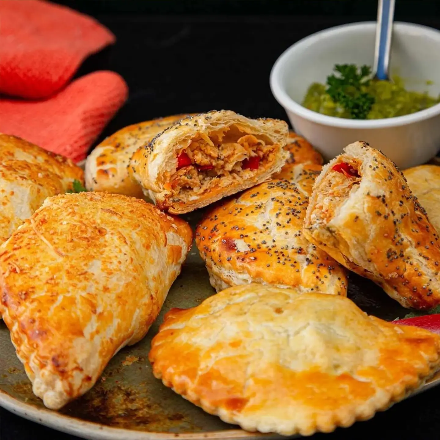 Empanadas de hojaldre horneadas con semillas de amapola rellenas de pollo desmechado y pimentón.