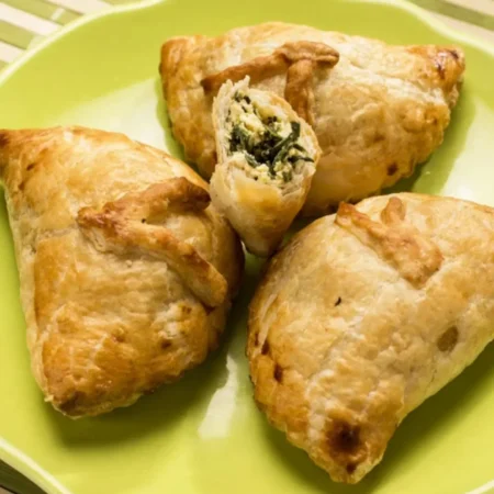 Empanadas de hojaldre horneadas rellenas de espinaca fresca y queso ricotta en plato verde.