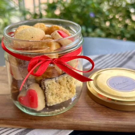 Frasco de vidrio con galletas surtidas artesanales de mantequilla decoradas y cinta roja de regalo.