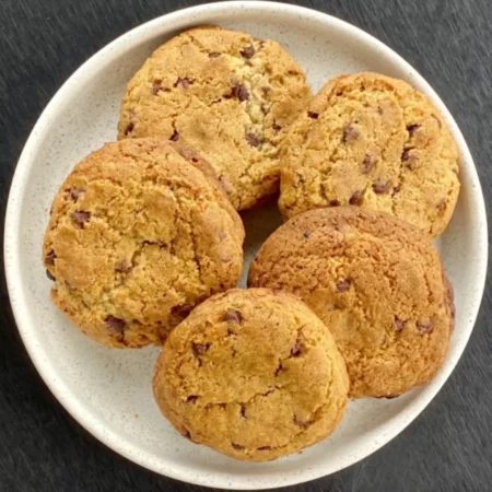 Galletas artesanales doradas con chispas de chocolate servidas en un plato blanco cerámico.