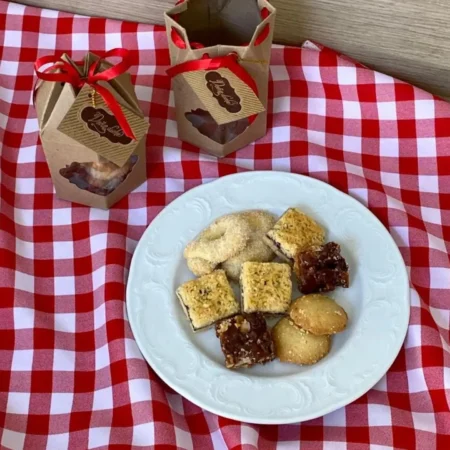 Plato con variedad de galletas artesanales surtidas y cajas para regalo con lazo rojo.
