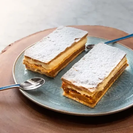 Dos porciones de milhoja artesanal de hojaldre crocante con arequipe, crema y azúcar glass.