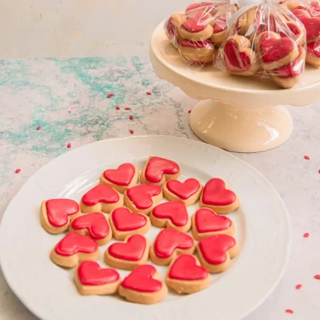 Plato con mini galletas artesanales en forma de corazón decoradas con glaseado rojo.