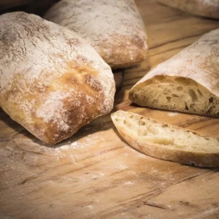 Pan ciabatta artesanal rústico en rebanadas con miga aireada sobre tabla de madera.