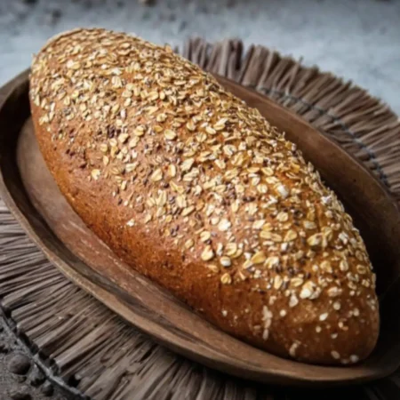 Hogaza de pan artesanal cubierta con hojuelas de avena y semillas en bandeja de madera.