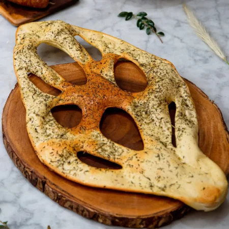 Pan artesanal en forma de hoja con cortes decorativos y cobertura de hierbas finas.