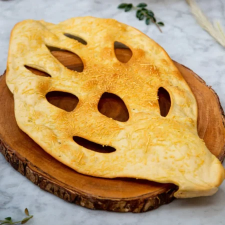 Pan artesanal en forma de hoja gratinado con queso parmesano sobre tabla de madera.