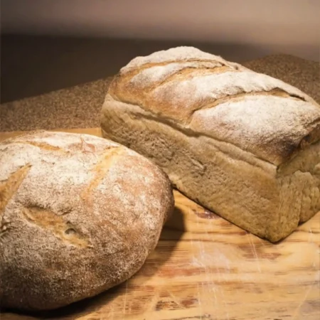Pan de miche artesanal de masa madre y hogaza horneada en superficie de madera.