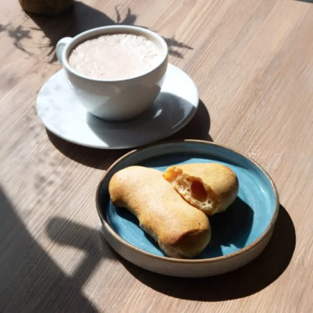 Pandeyucas horneados dorados en plato azul junto a una taza de chocolate caliente.