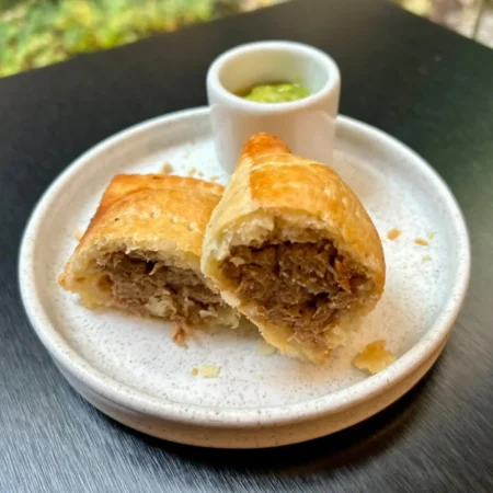 Pastel de carne hojaldrado artesanal partido a la mitad con salsa verde en plato cerámico.