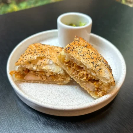 Pastel de pollo hojaldrado artesanal partido a la mitad con semillas de amapola en plato cerámico.