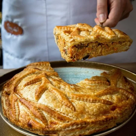 Pastel familiar de hojaldre dorado servido en porción con abundante relleno de pollo y champiñones.