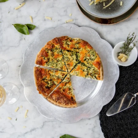 Quiche artesanal de espinaca y ricotta cortado en porciones sobre plato metálico plateado.