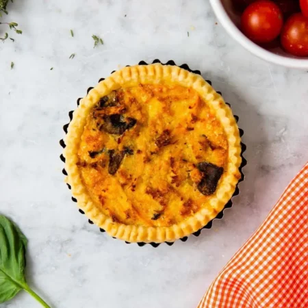 Quiche individual de pollo y champiñones con borde rizado dorado en molde tartero.