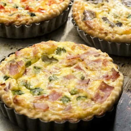 Quiche individual de tocineta, jamón y finas hierbas en molde metálico acanalado.