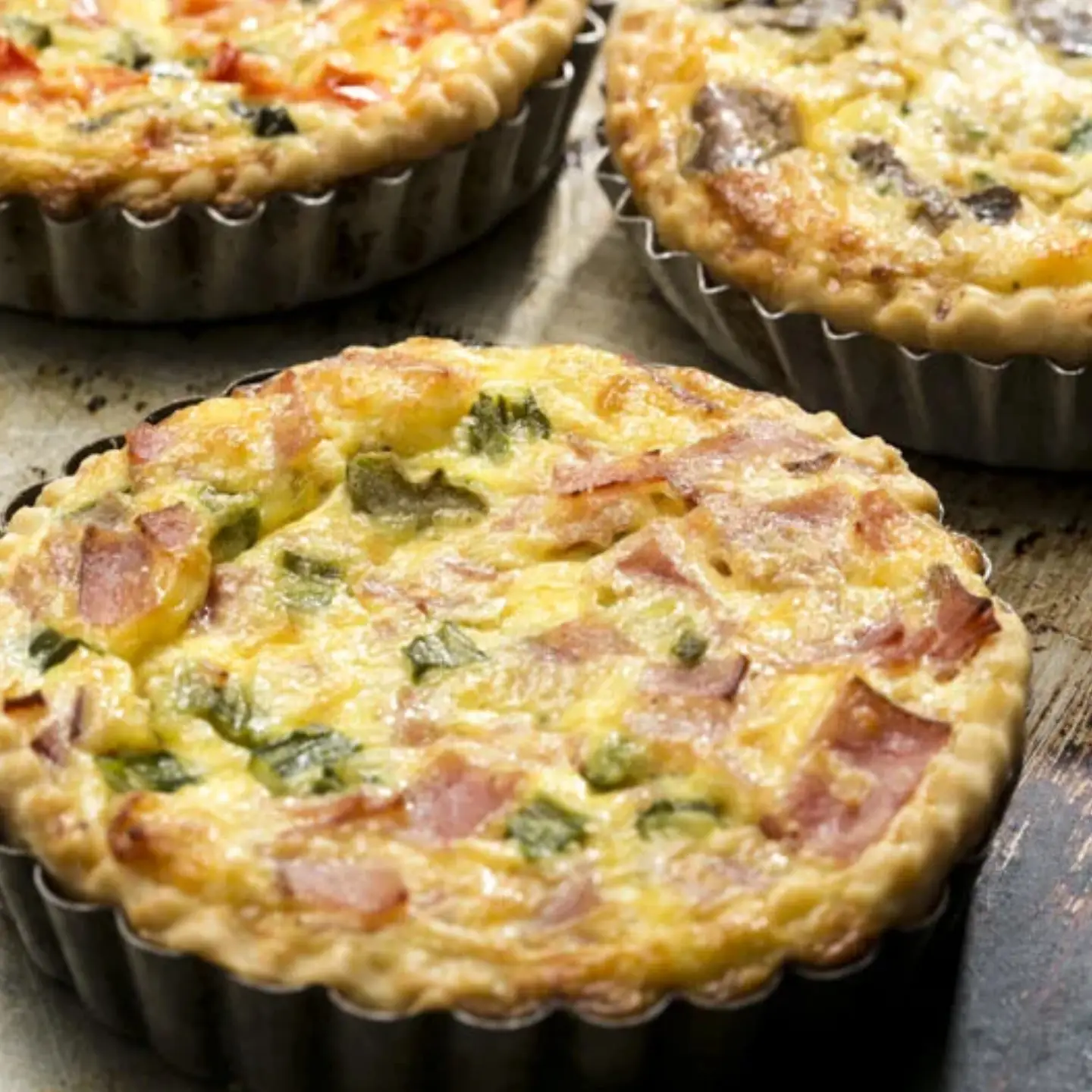 Quiche individual de tocineta, jamón y finas hierbas en molde metálico acanalado.