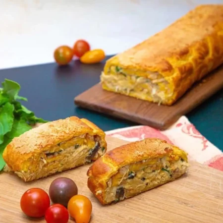 Rollo de soufflé dorado de pollo y champiñones rebanado en tabla de madera.