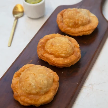 Tres sombreritos fritos y dorados de papa y carne sobre una tabla de madera.