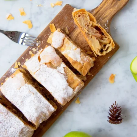 Strudel de manzana artesanal en rebanadas sobre tabla de madera espolvoreado con azúcar glass.