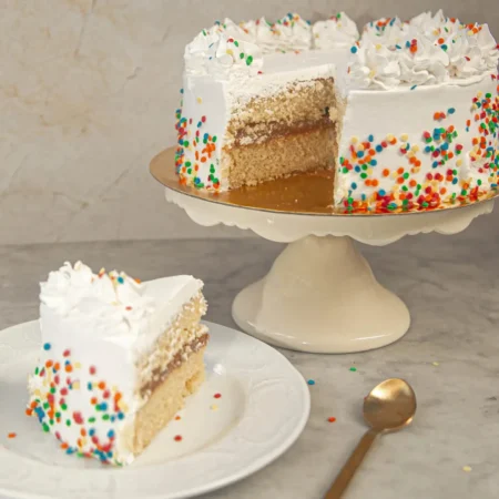 Torta artesanal blanco clásico con relleno de arequipe, cobertura blanca y chispas de colores.