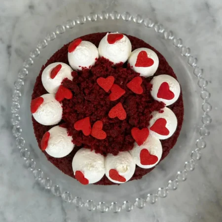 Torta Red Velvet artesanal vista superior decorada con rosetas de queso crema y corazoncitos rojos.
